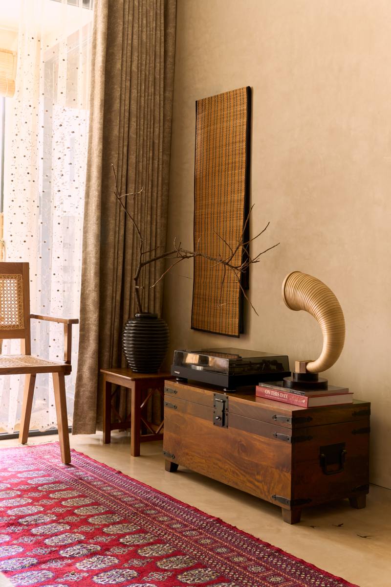 Vintage timber trunk holding a record player, a bamboo gramophone horn and books, with a woven wall panel and a branch in a black vase