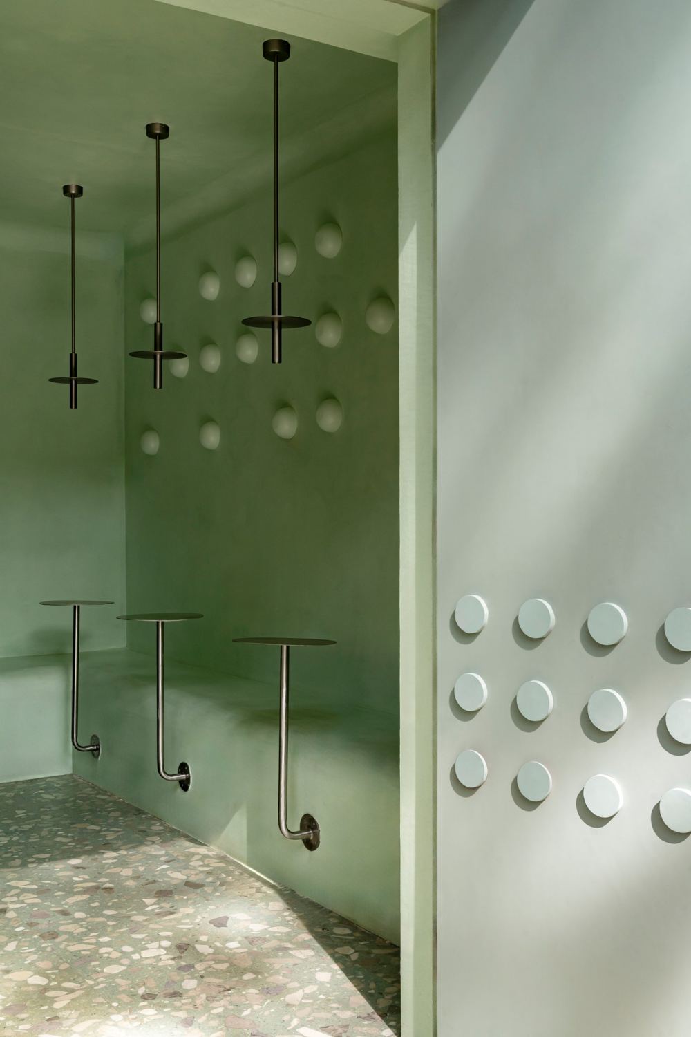 Mint plaster niche with bronze pendants, domed wall lights and wall-mounted steel tables, beside the door studded with raised discs