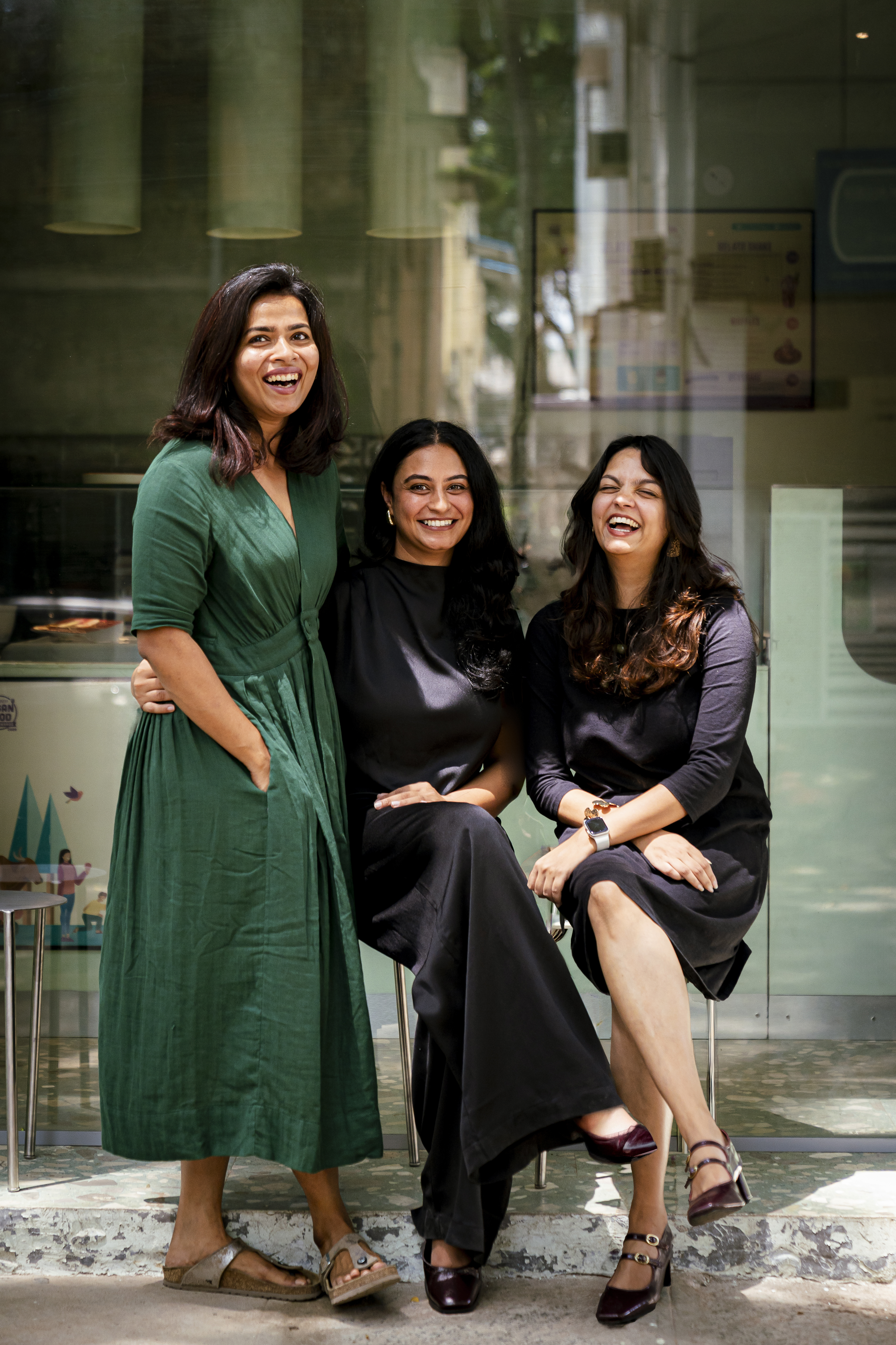 Vasundhara Shiva Kumar, Kavya Narayana and Sayli Khadilkar laughing together outside a mint-green storefront