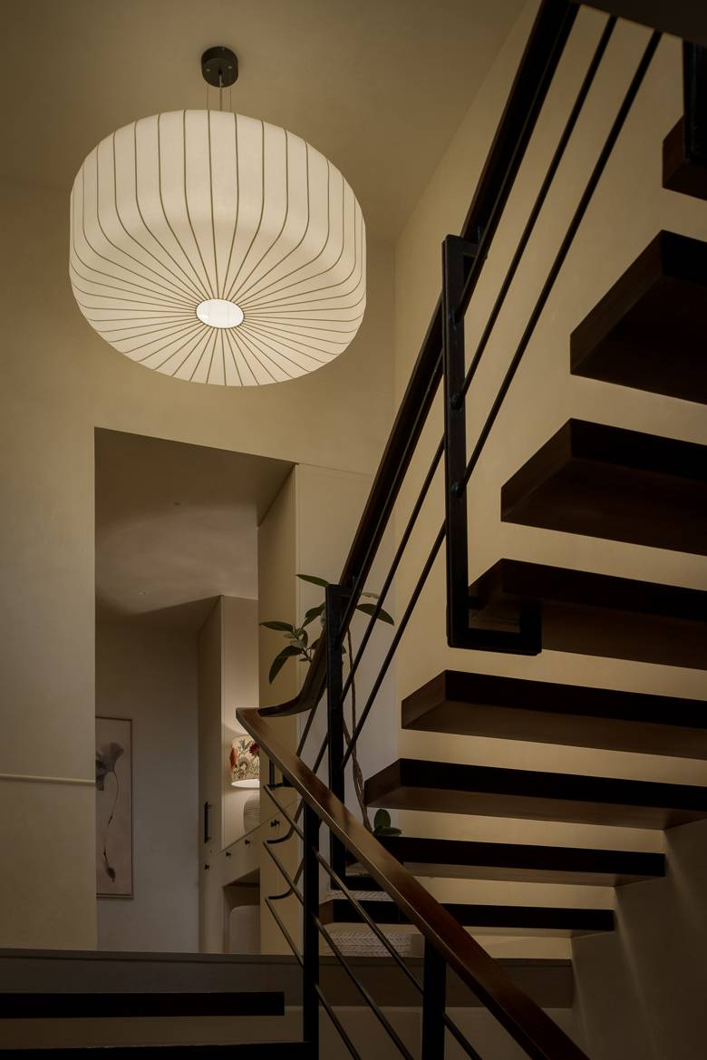 Staircase with floating timber treads, a black railing and a large pleated pendant light