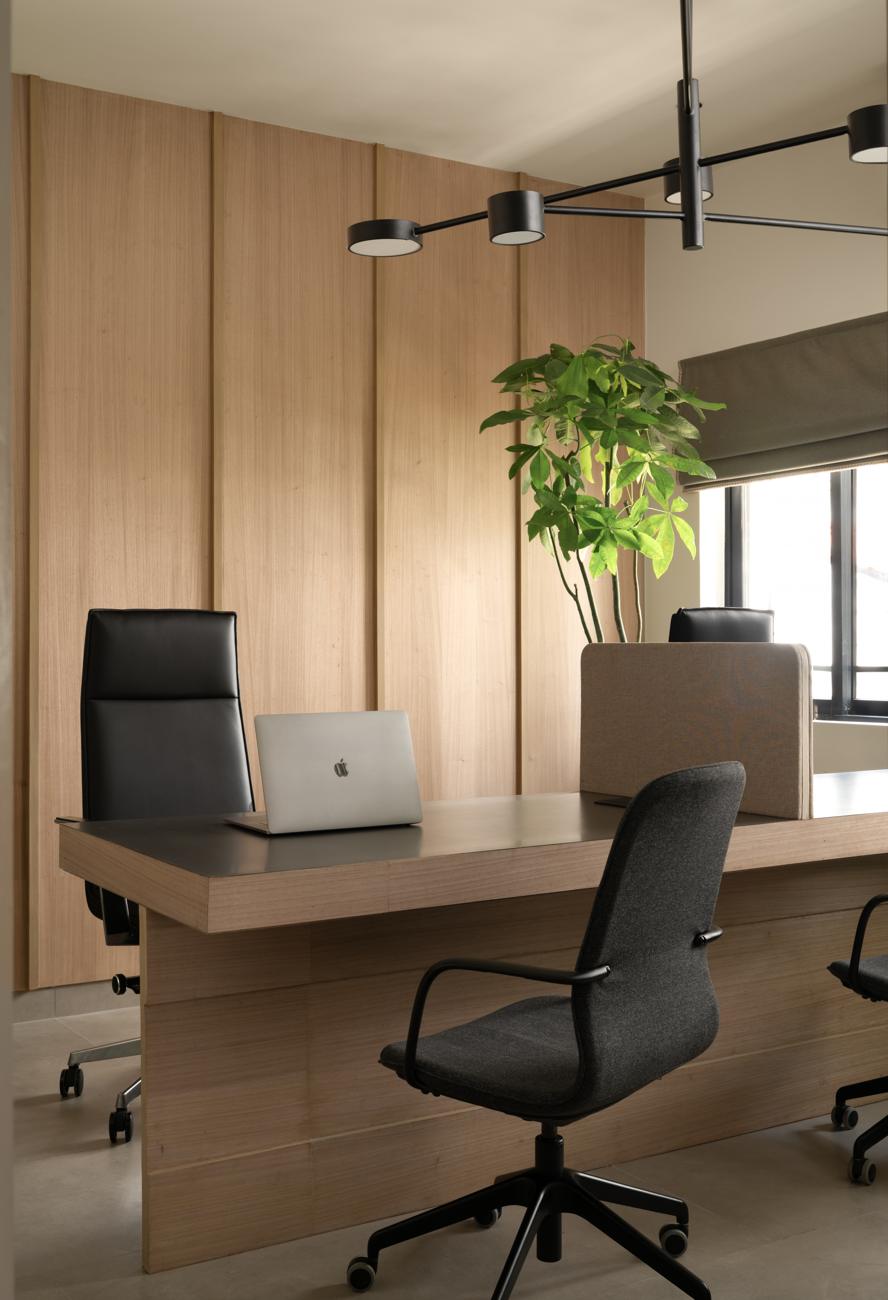 Soft Steel office with a desk, laptop and leather chair against a wood-panelled wall, a black disc chandelier above and a potted plant by the window