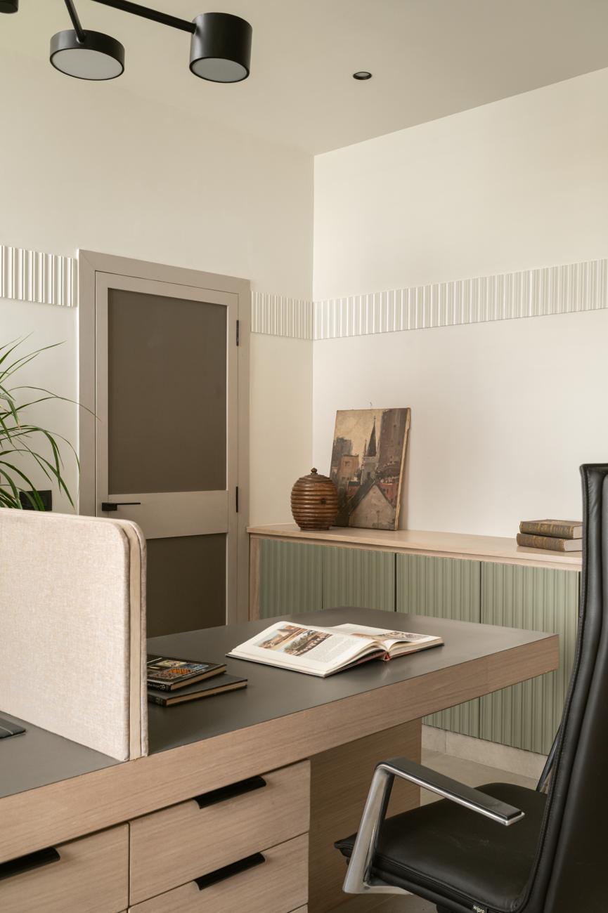 Desk with a fabric screen and an open book, a grey-framed door, and a green fluted cabinet topped with an antique painting and a wooden pot