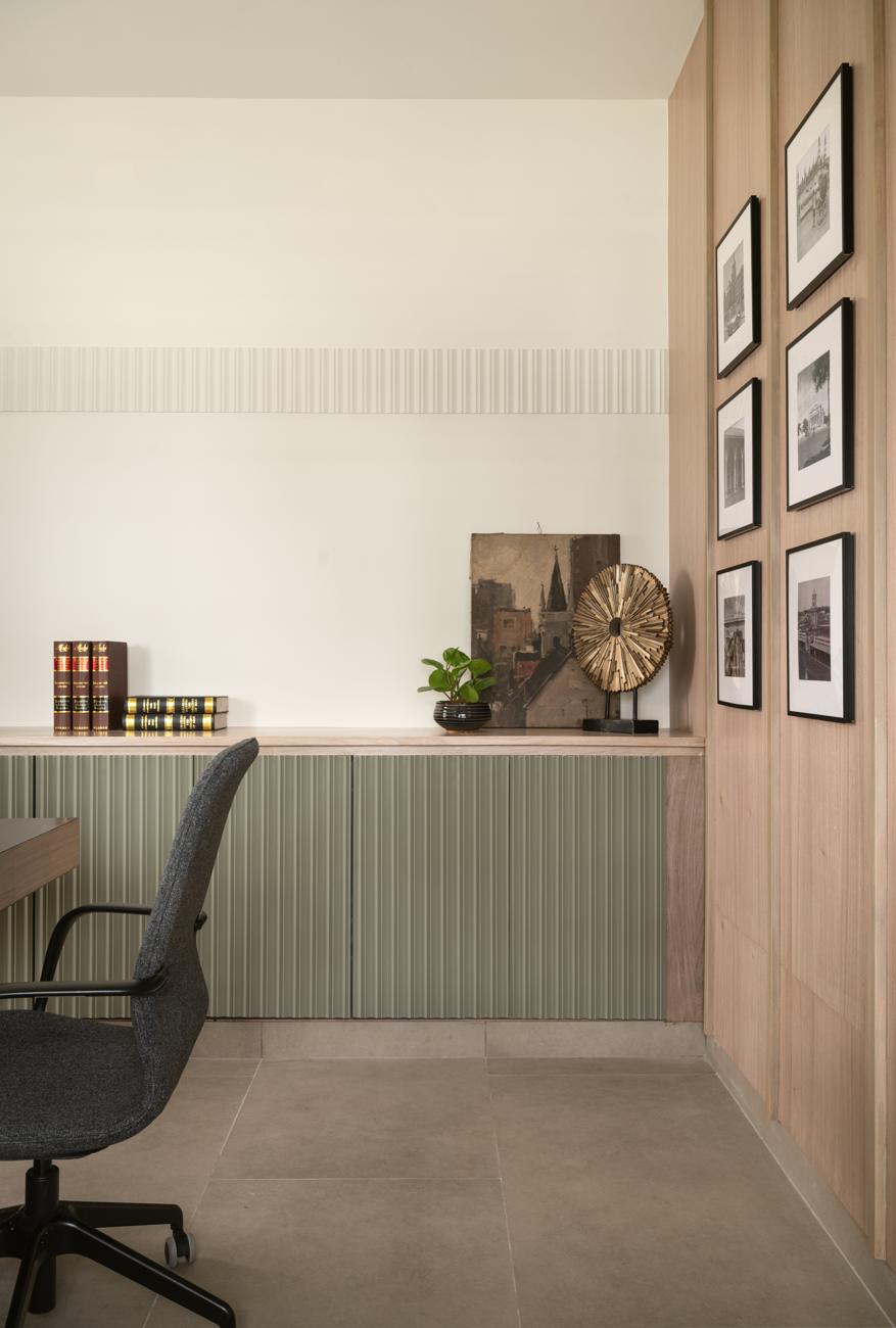 Corner of the office with a green fluted cabinet, framed black-and-white prints on a wood-panelled wall and a grey chair