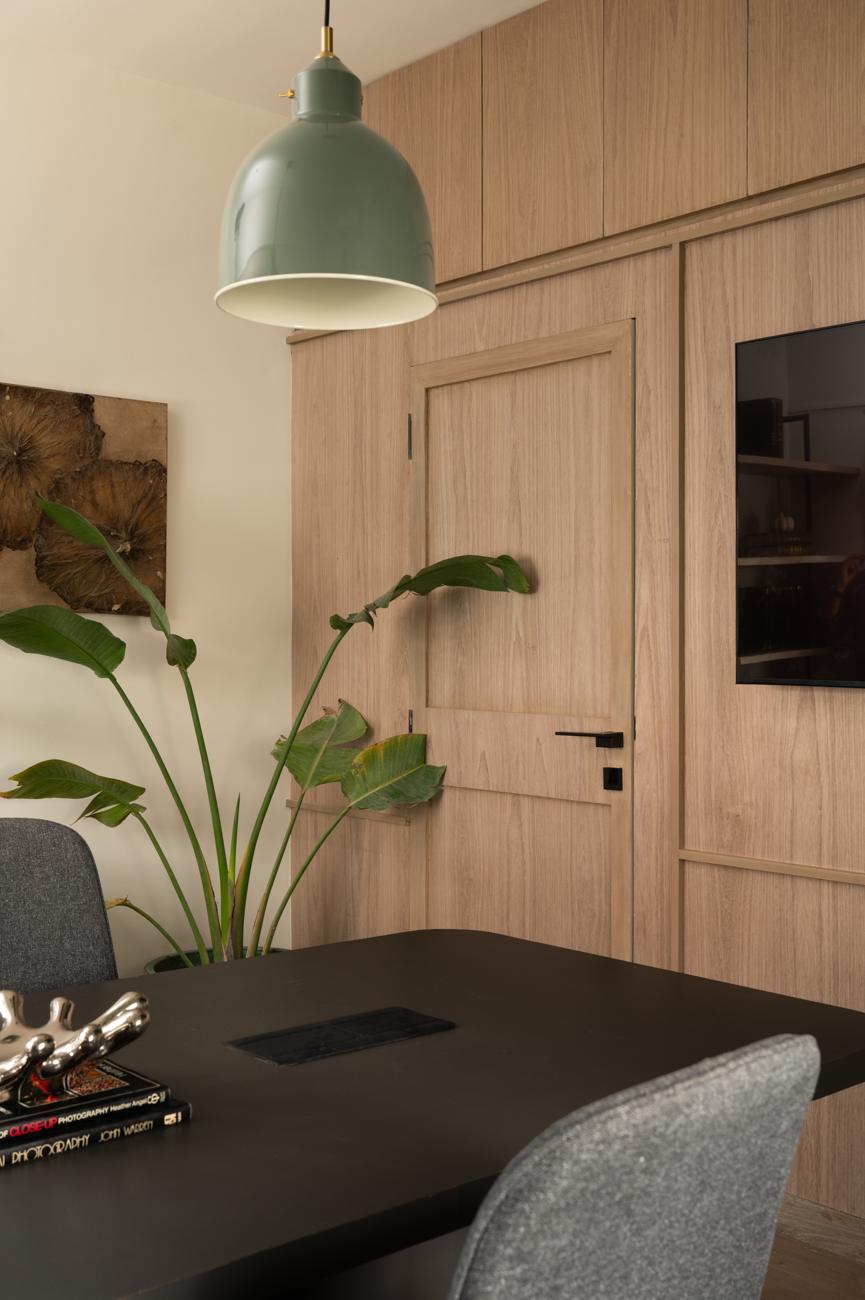 Meeting room with a door set into wood panelling, a green pendant lamp, a leafy plant and a dark table with grey chairs