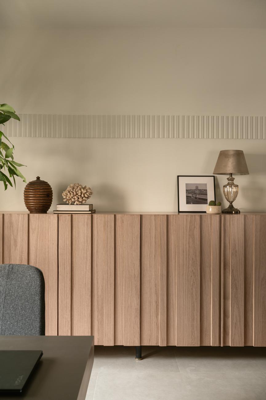Long fluted wood sideboard topped with a wooden pot, coral, a framed print and a table lamp