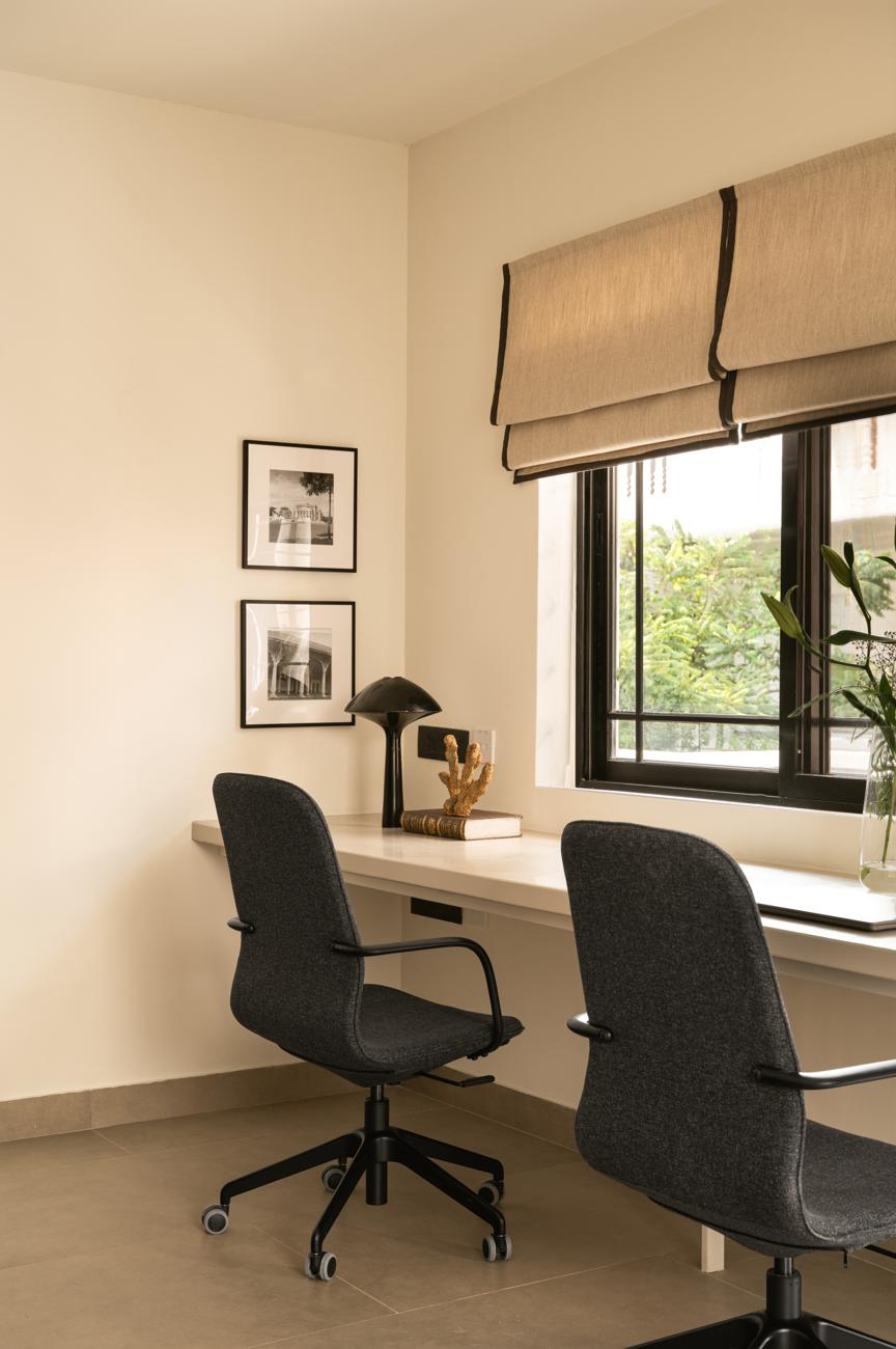 Window desk with two grey chairs, a black mushroom lamp, framed prints and a roman blind