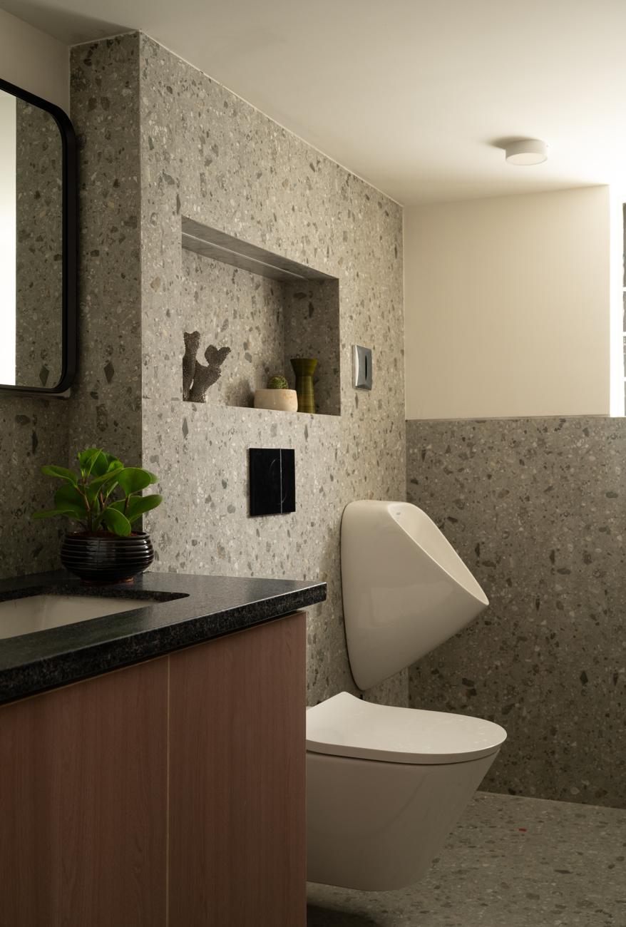Bathroom with grey terrazzo walls, a recessed niche, a wood vanity with a black granite top and wall-hung fittings