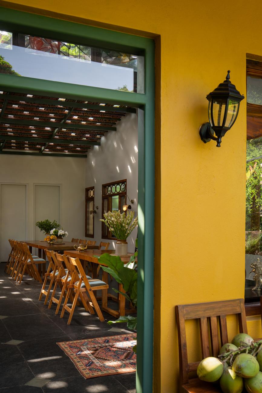 View through a green door frame from the yellow-walled terrace into the dining room with a tiled ceiling and folding chairs