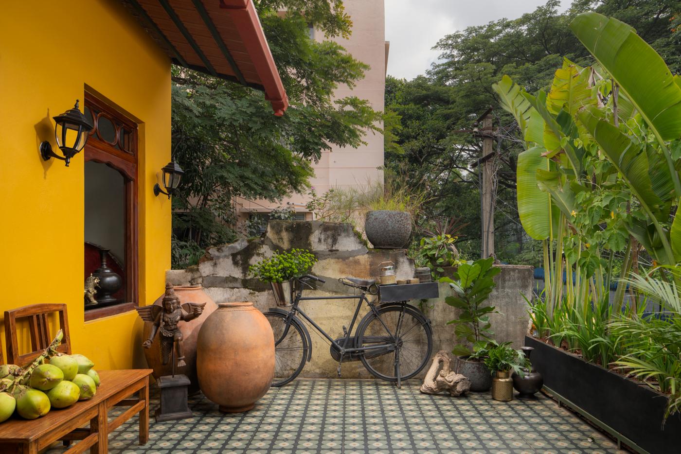 Courtyard at the threshold of the dining room with a yellow wall, terracotta pots and a bicycle against a weathered wall