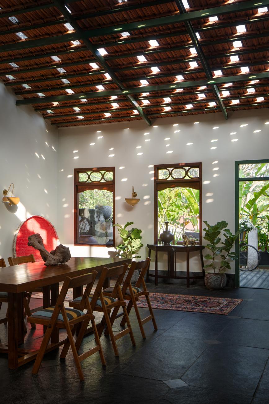 Dining room with a clay-tile ceiling lit by skylights, a long table, folding chairs, a red woven basket and an open green door