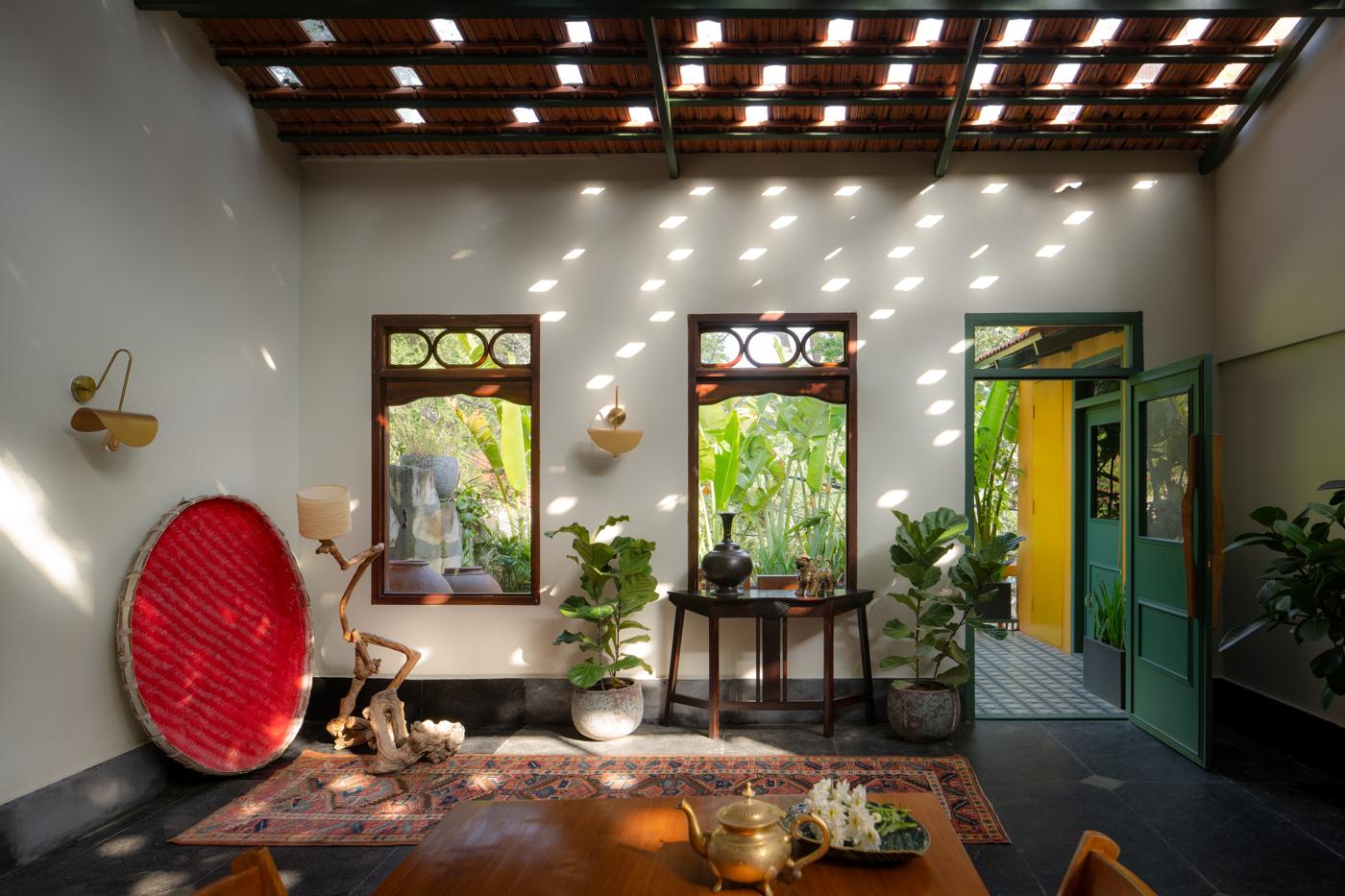 Dining room seen from one end, with a red woven basket, a driftwood piece on the table, windows and an open green door to the terrace