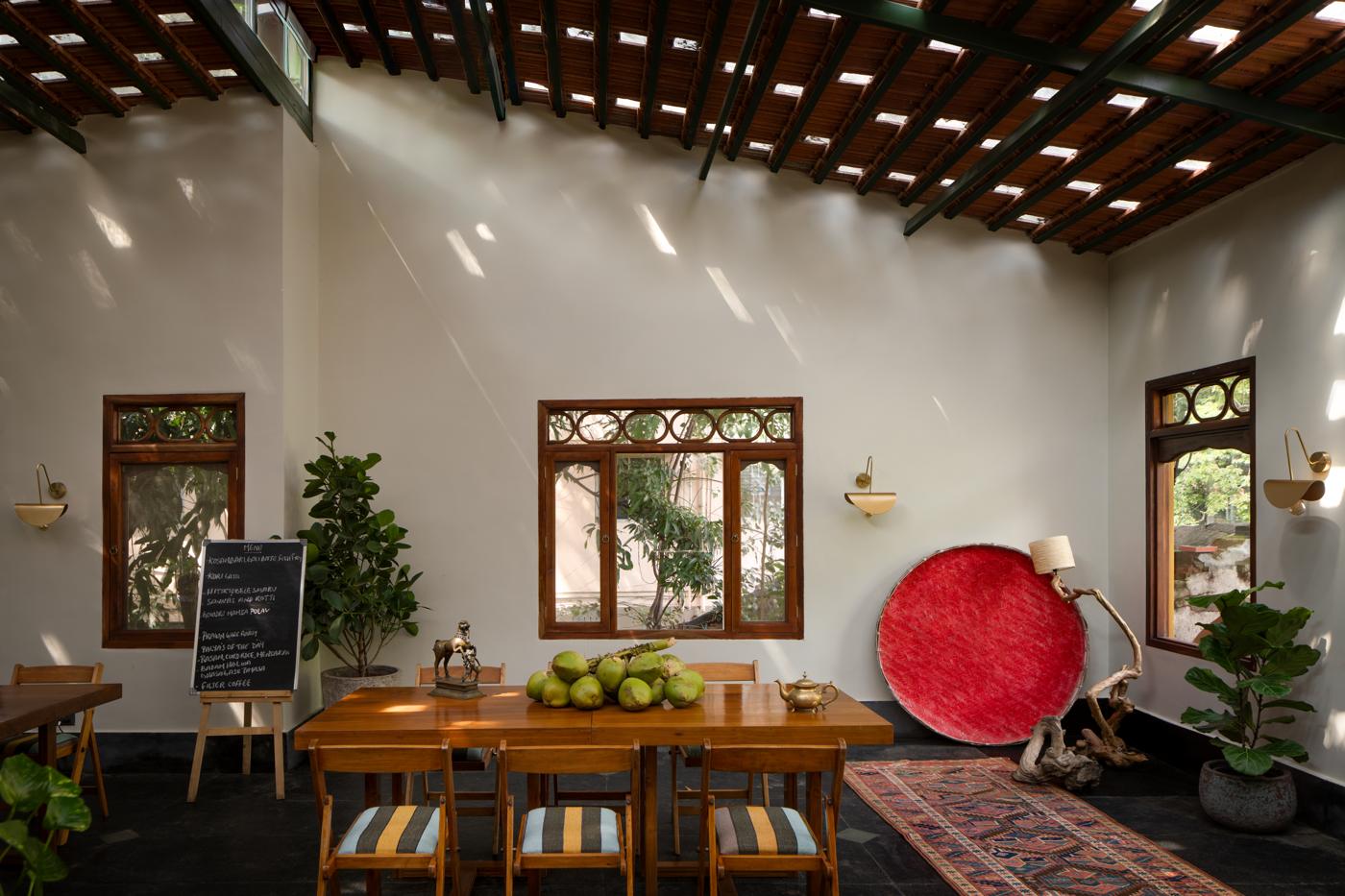 Long timber dining table with folding chairs, a red woven basket and a chalkboard under a tiled ceiling with skylights