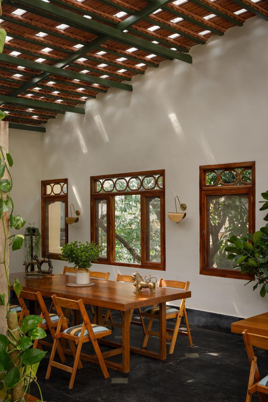 Dining room wall with carved timber windows, a long table, folding chairs and plants
