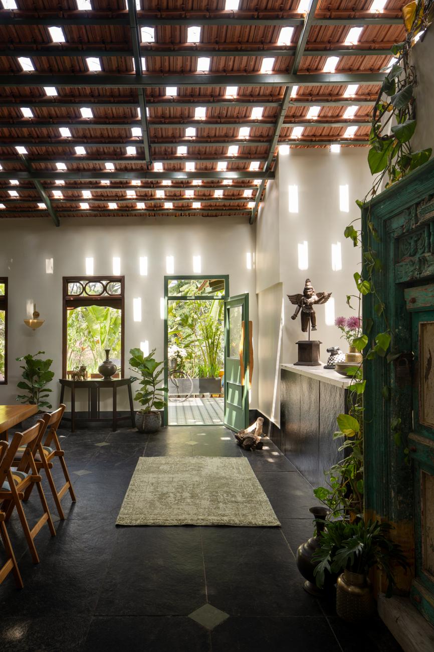 Long view through the dining room towards a green door, with a vintage rug, plants and an antique carved door