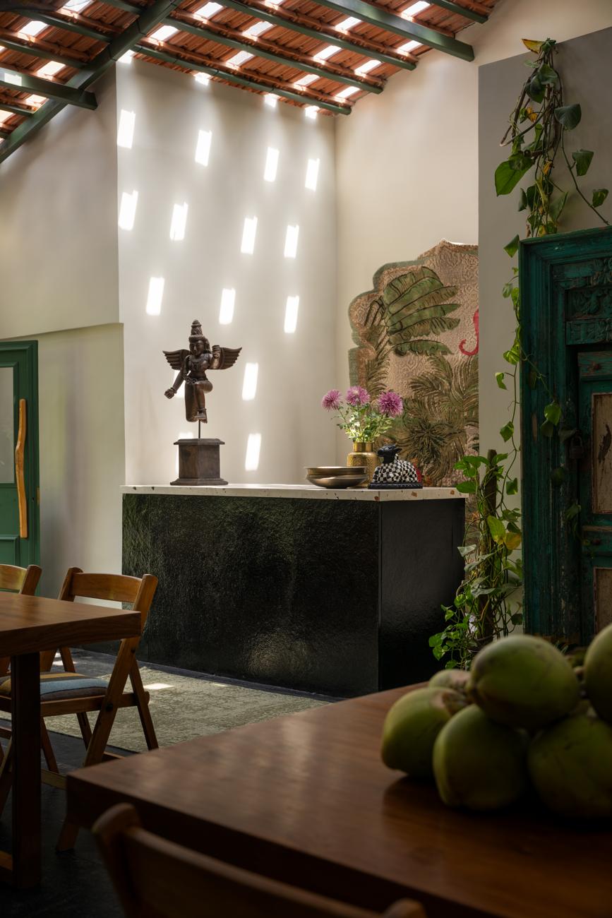 Dark stone bar counter with a carved wooden figure, flowers and a pile of green coconuts