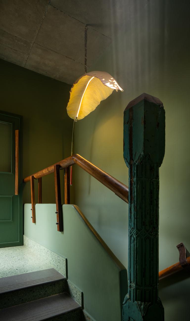 Staircase with an antique carved pillar, a timber handrail, green walls and a leaf-shaped pendant lamp