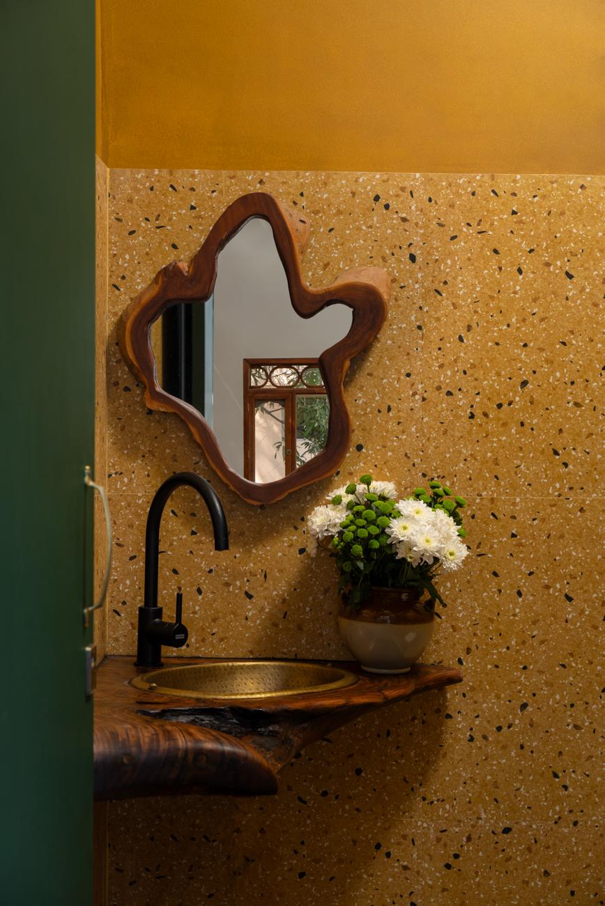 Powder room with a wavy-edged mirror, a copper basin, a black tap, white flowers and a warm terrazzo wall