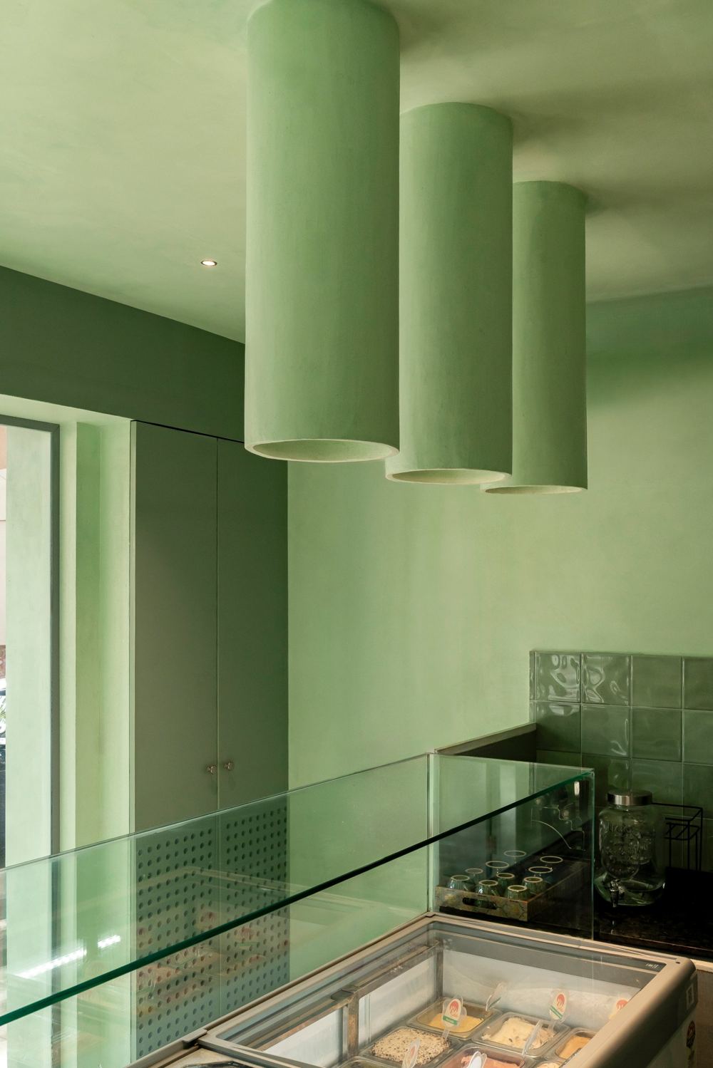 Three mint plaster cylinders hanging from the ceiling above a glass display counter and gelato freezer
