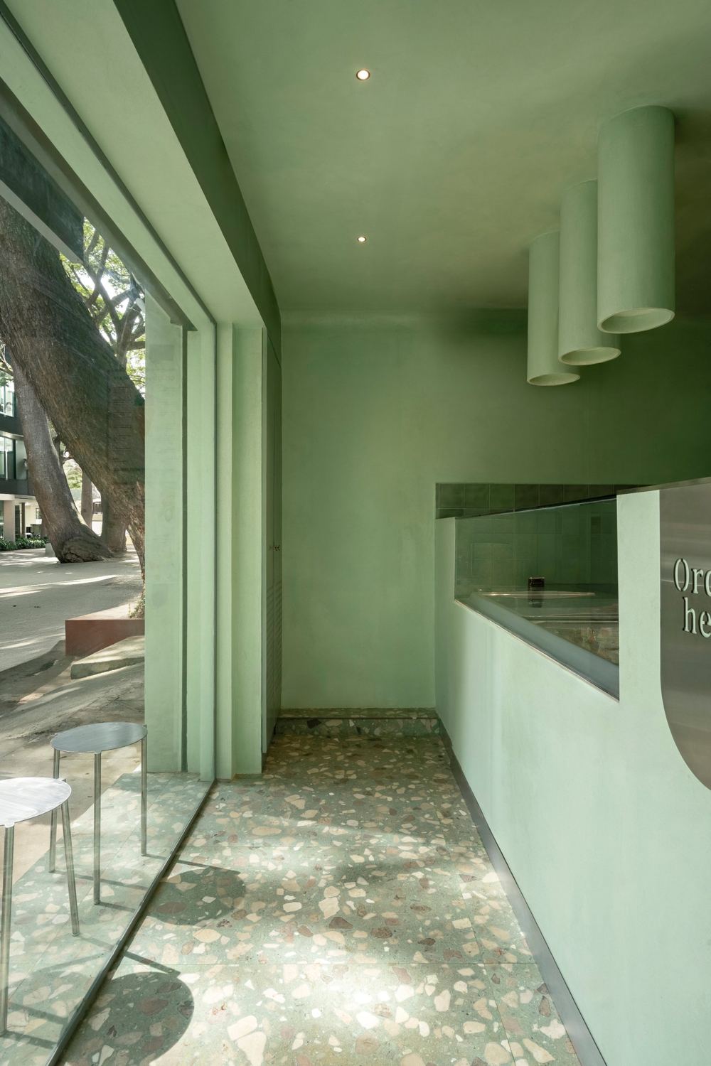Interior along the window with a large tree outside, plaster cylinder lights, a glass-topped counter and a terrazzo floor