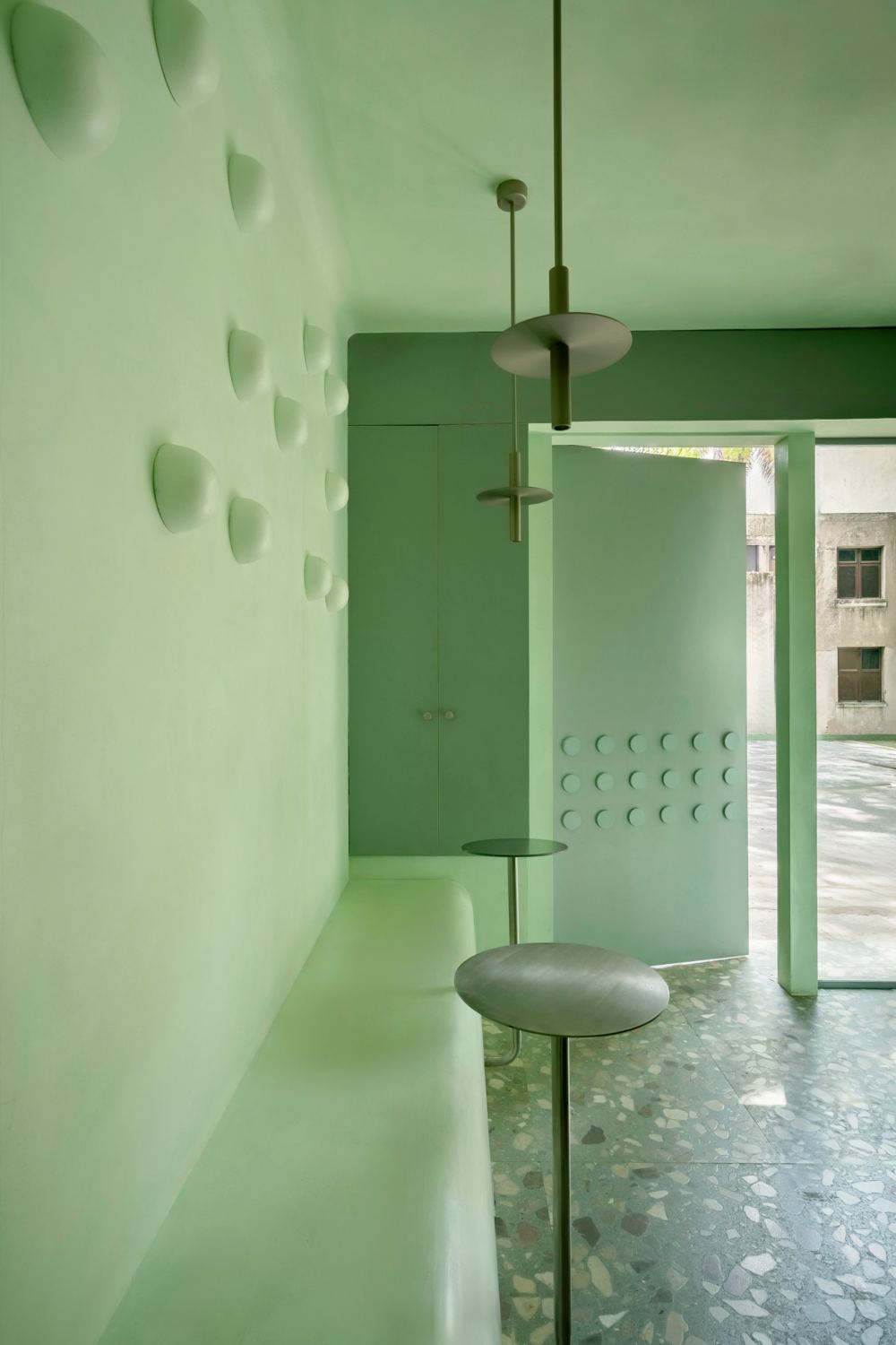 Built-in plaster bench along a wall of domed lights, steel tables and an open disc-studded door onto the street