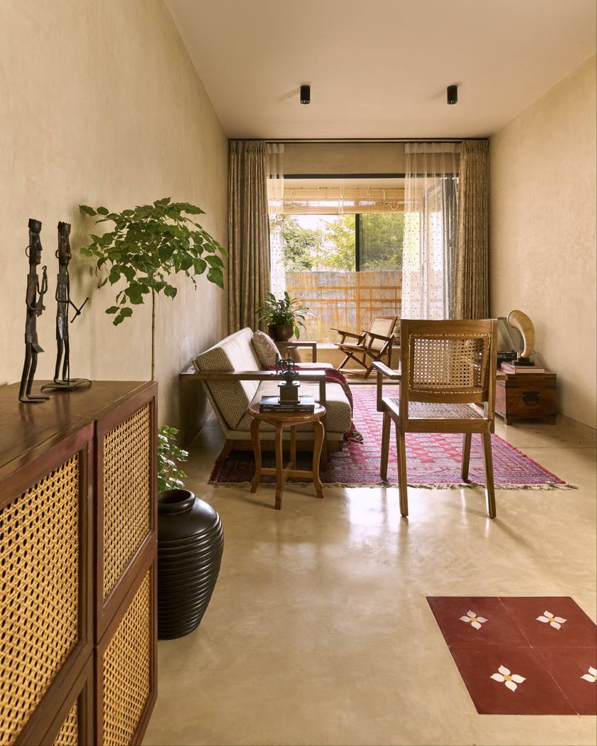 Long foyer leading to the living room, with a cane-fronted timber cabinet, bronze figures, a tall plant, a red rug and a balcony beyond