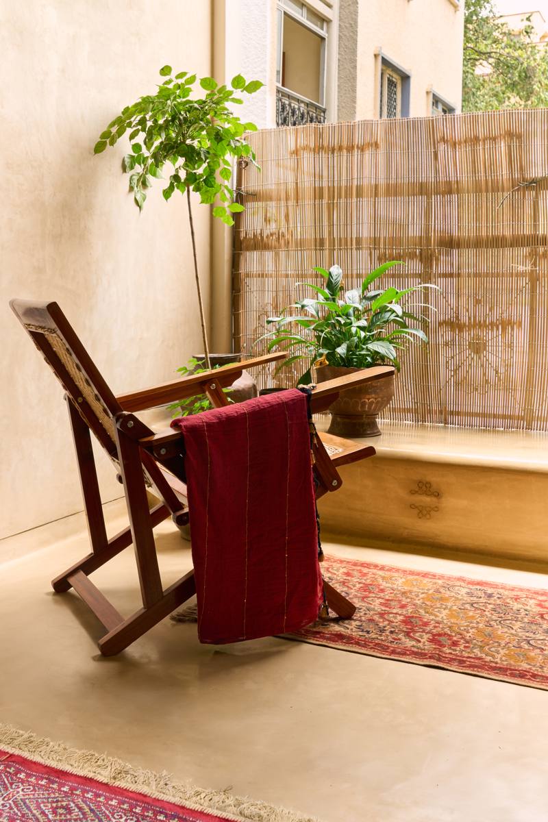 Balcony extension with a folding timber armchair draped in a red cloth, plants, a bamboo screen and a patterned rug