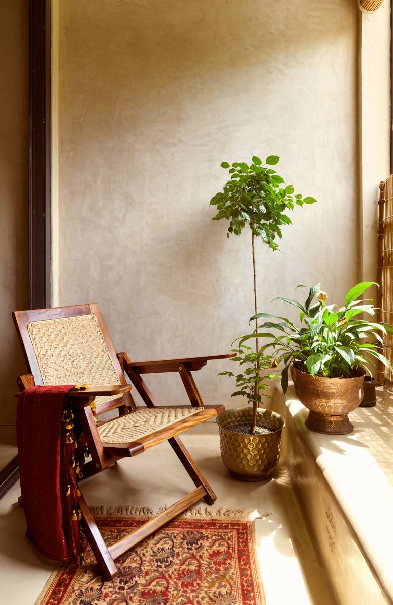 Folding armchair with a woven seat and a red cloth beside potted plants and brass planters on a warm plastered balcony