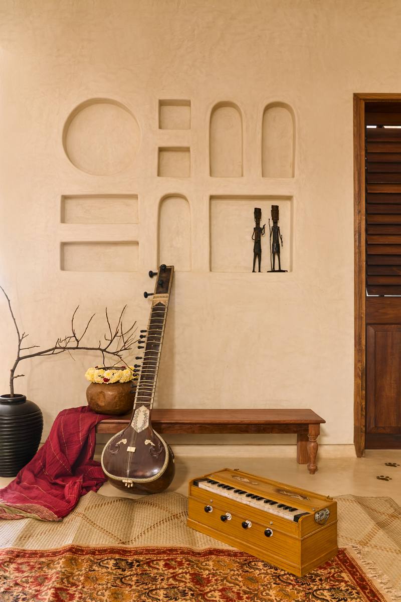 Music corner with a sitar, a harmonium, a low timber bench, a brass pot of marigolds and sculpted wall niches holding bronze figures