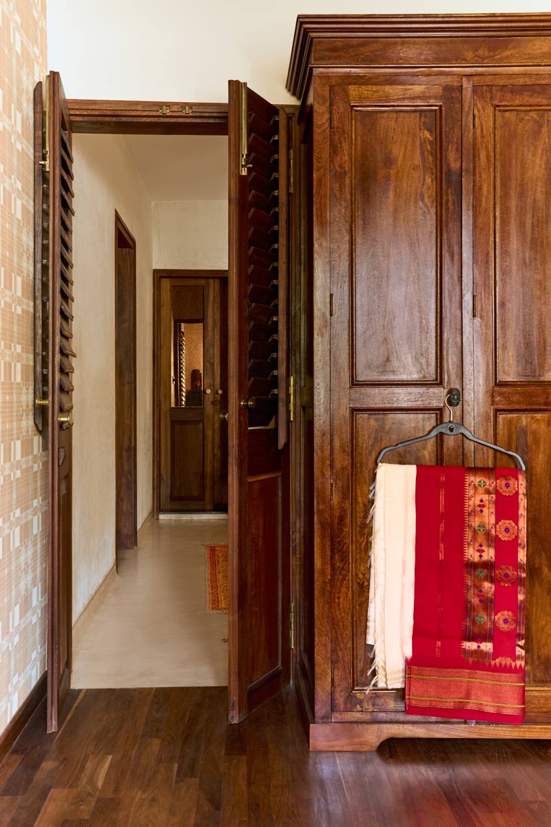 View from the bedroom through louvered doors towards the common area, with an antique timber wardrobe and a red saree on a hanger
