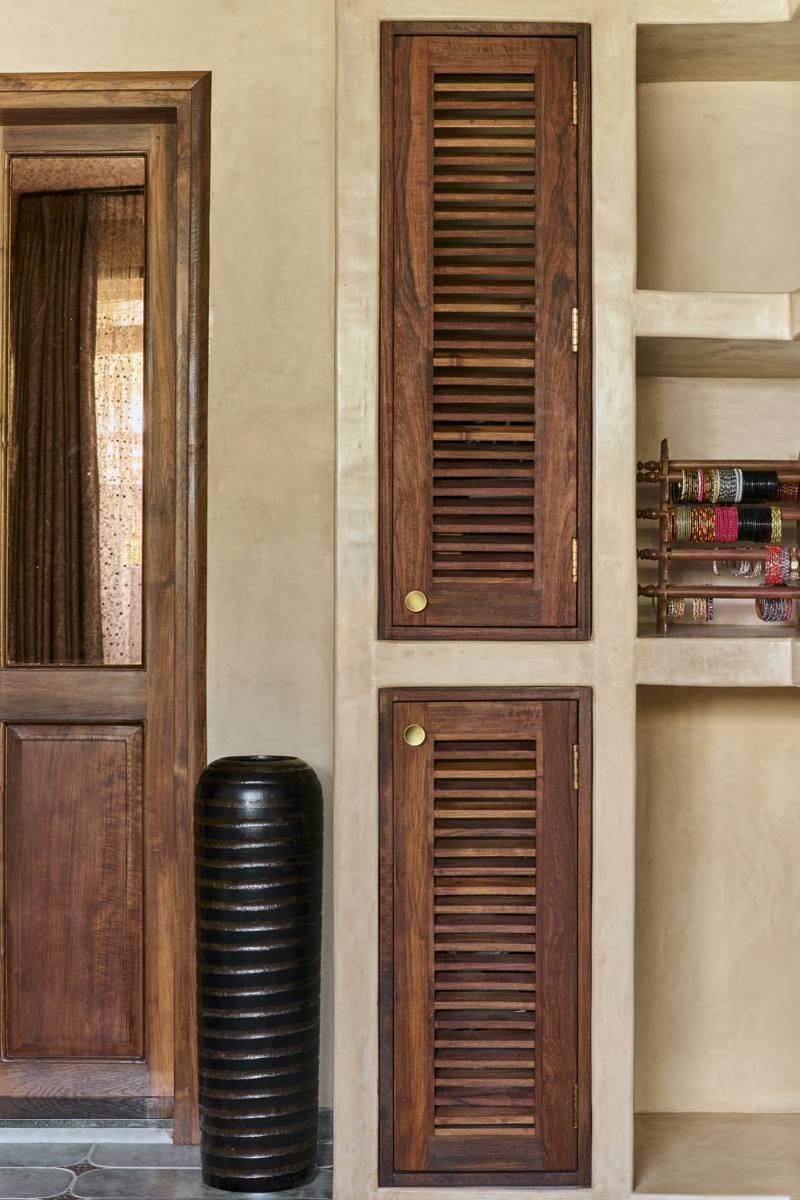 Louvered timber cabinet doors set in plaster beside a black ribbed vase, an antique mirror door and shelves of bangles
