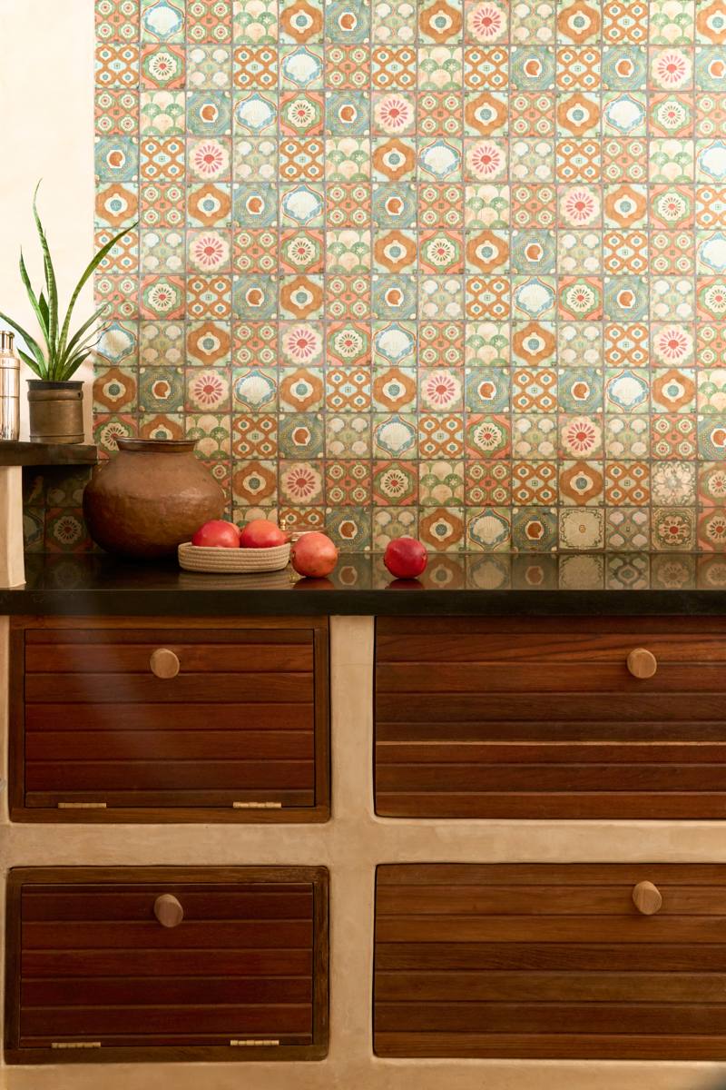 Kitchen counter with a black stone top, a hand-painted shell and floral tile wall, timber shutters with round knobs, a copper pot and pomegranates