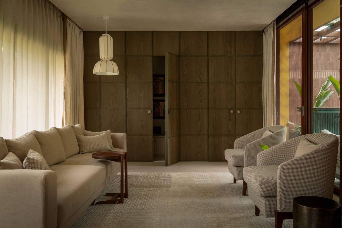 Living room with a sofa and tweed armchairs facing a wall of oak panelling, with one door open to a shrine cabinet