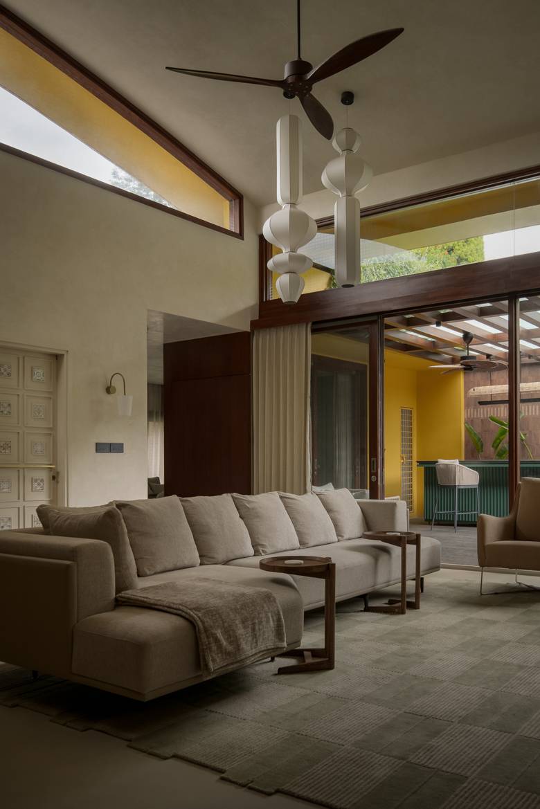 Double-height living room with a long sofa, two tall white pendant lights, a ceiling fan and a clerestory window with a yellow reveal, opening onto a terrace