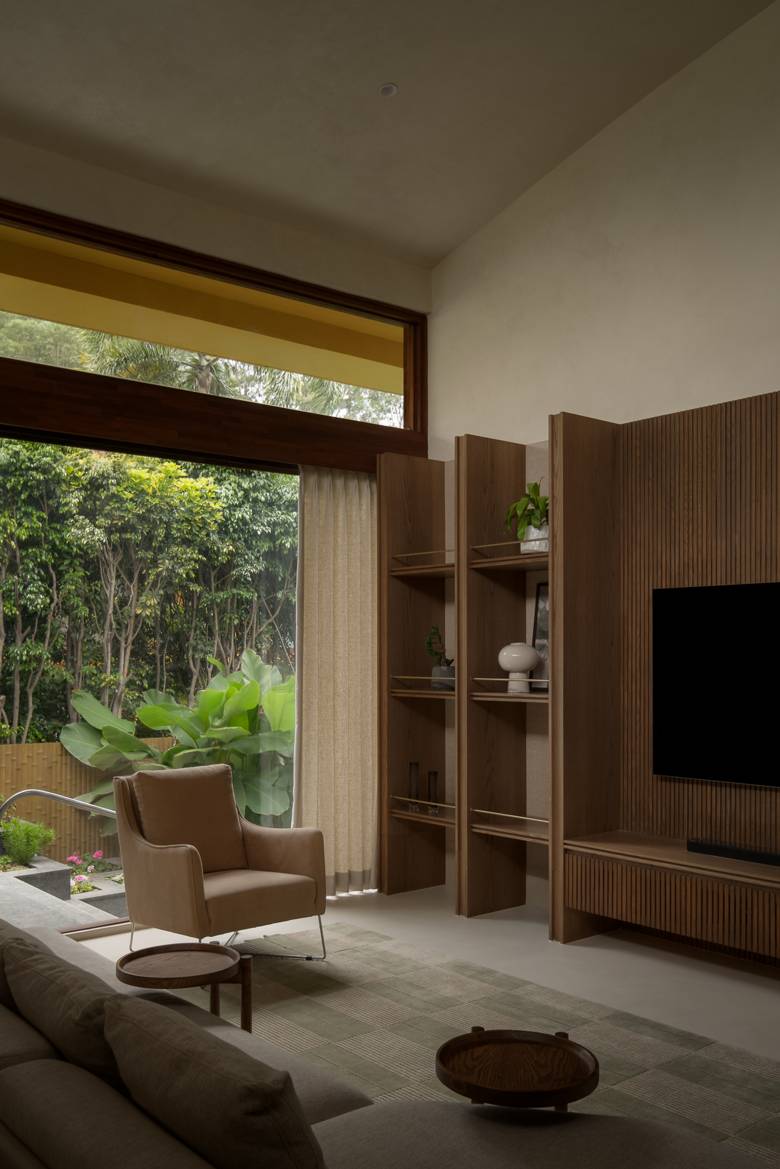 Living room corner with a leather armchair by a tall garden window, open timber shelving and a ribbed timber TV wall
