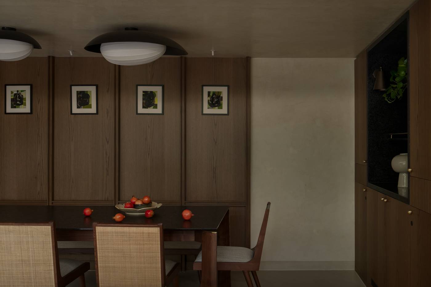 Dining area with four framed abstract artworks on oak panelling, a bowl of pomegranates and a dark stone niche with a plant