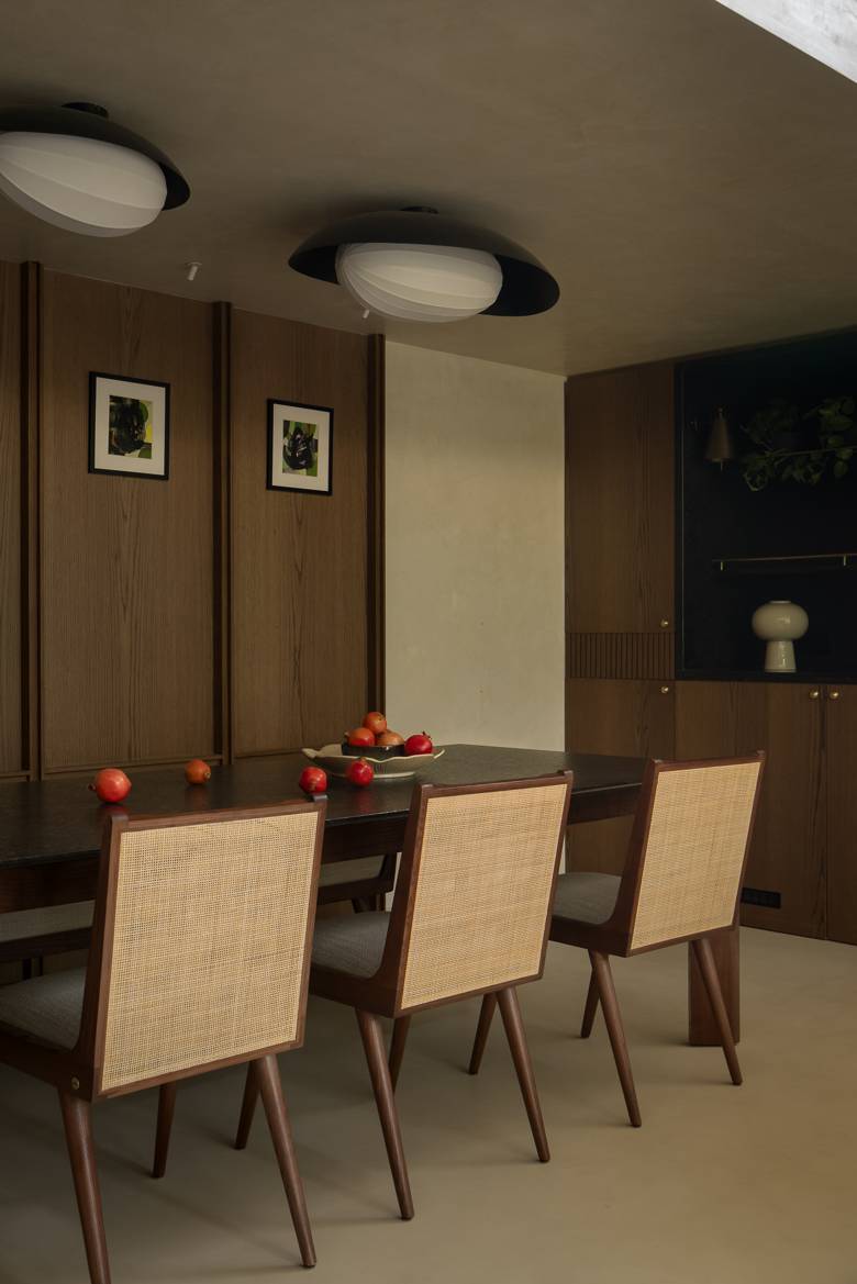 Close view of cane-backed dining chairs at a dark stone-topped table, with framed artworks on an oak panelled wall
