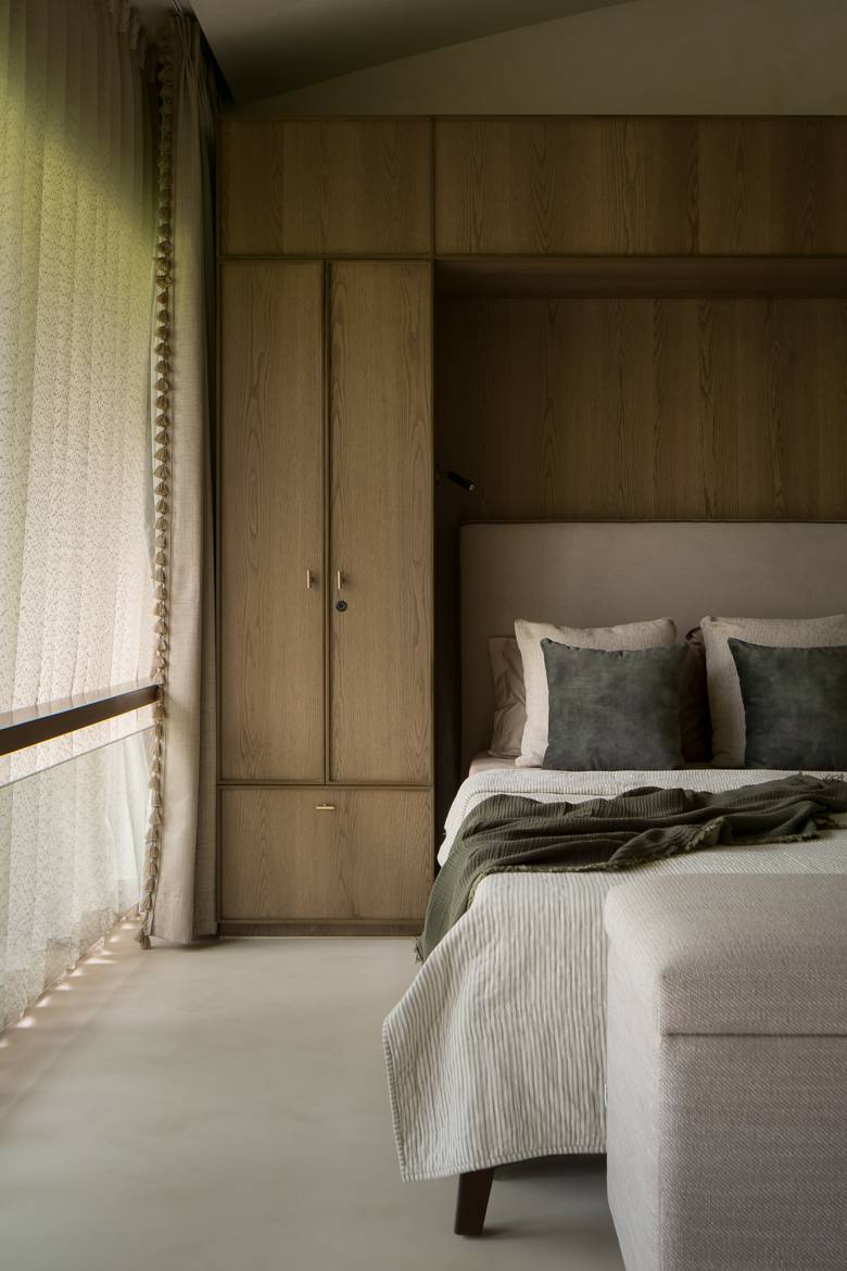 Bedroom with an oak wardrobe and headboard wall, a bed with a green throw and a sheer tasselled curtain