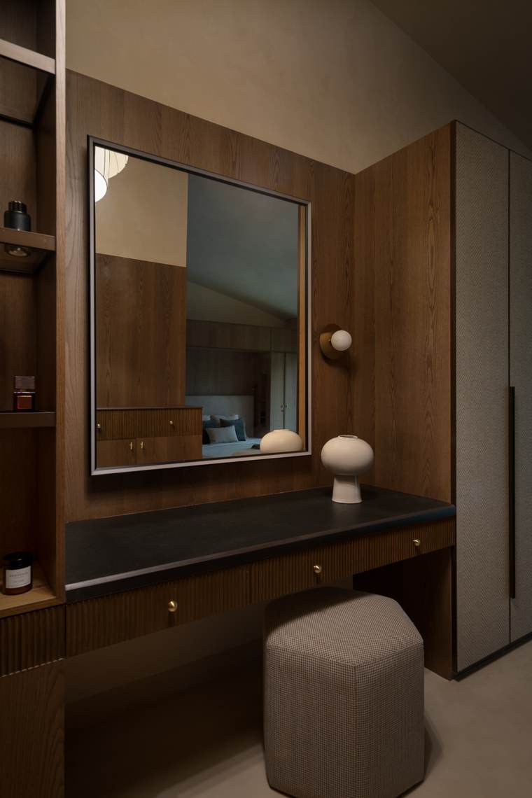 Dressing table with a black counter and fluted drawers, a large framed mirror, a round white vase, a hexagonal houndstooth stool and a herringbone wardrobe