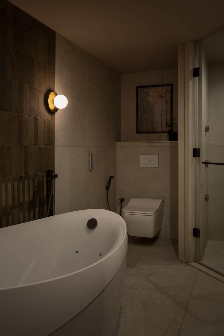 Bathroom with a freestanding white tub, a brass globe wall light, green vertical tiles, a wall-hung toilet and a glass shower door