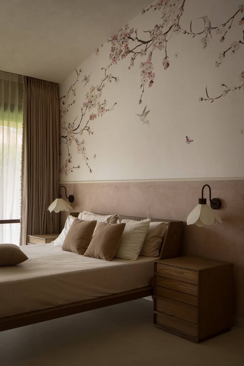 Bedroom with cherry-blossom and hummingbird wallpaper above a pink plaster panel, flower-shaped wall lights and timber bedside tables