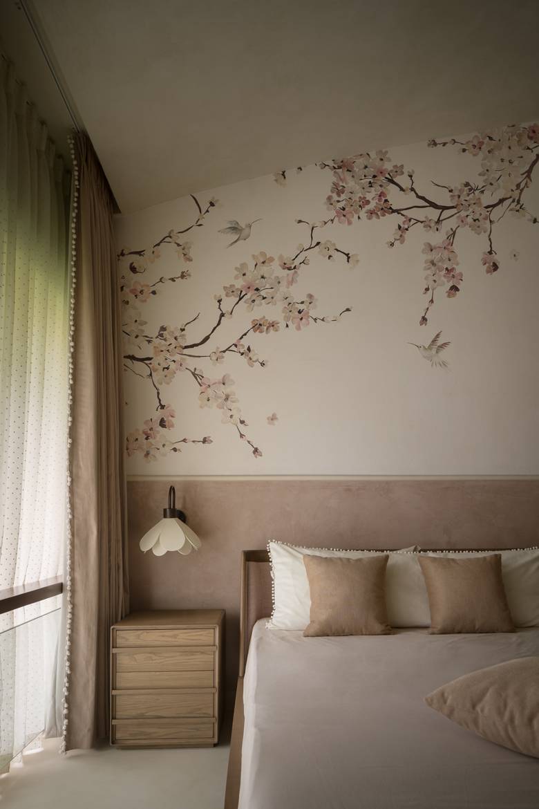 Bedroom wall with cherry-blossom wallpaper, a petal-shaped wall light and a timber bedside chest beside a sheer curtain
