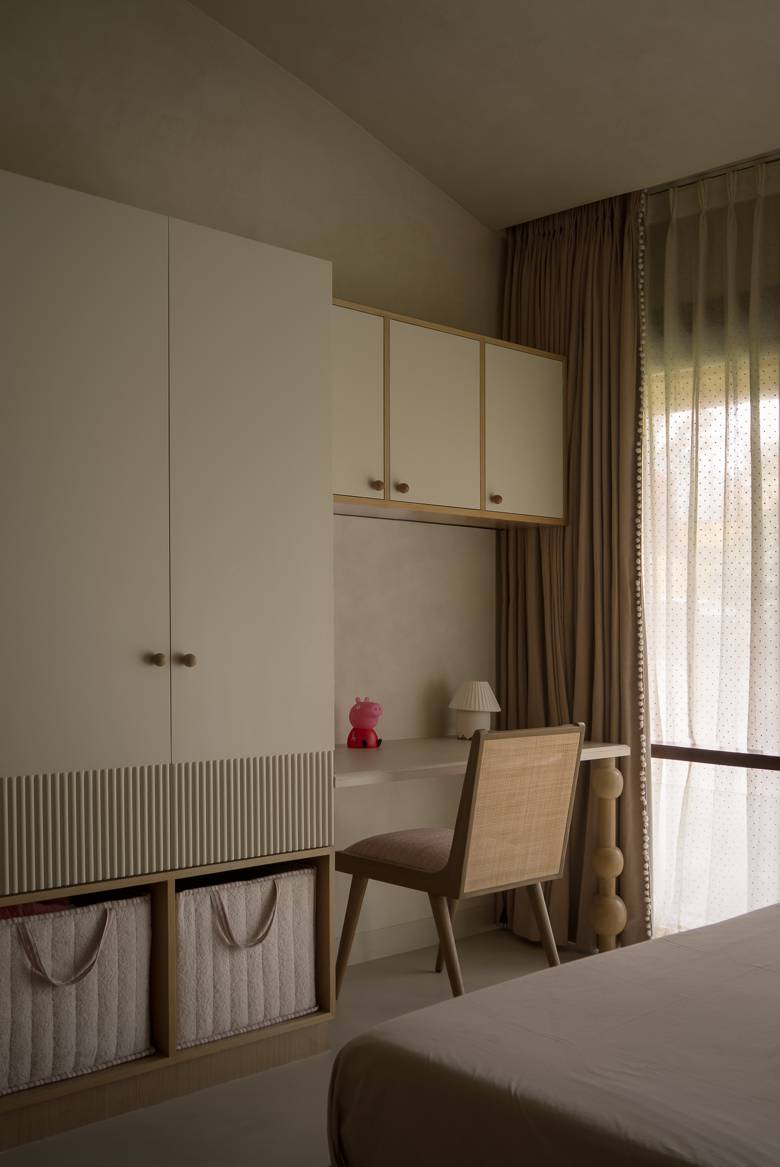 Child's bedroom with a white wardrobe with fluted panels, a built-in desk with a cane-backed chair and storage baskets