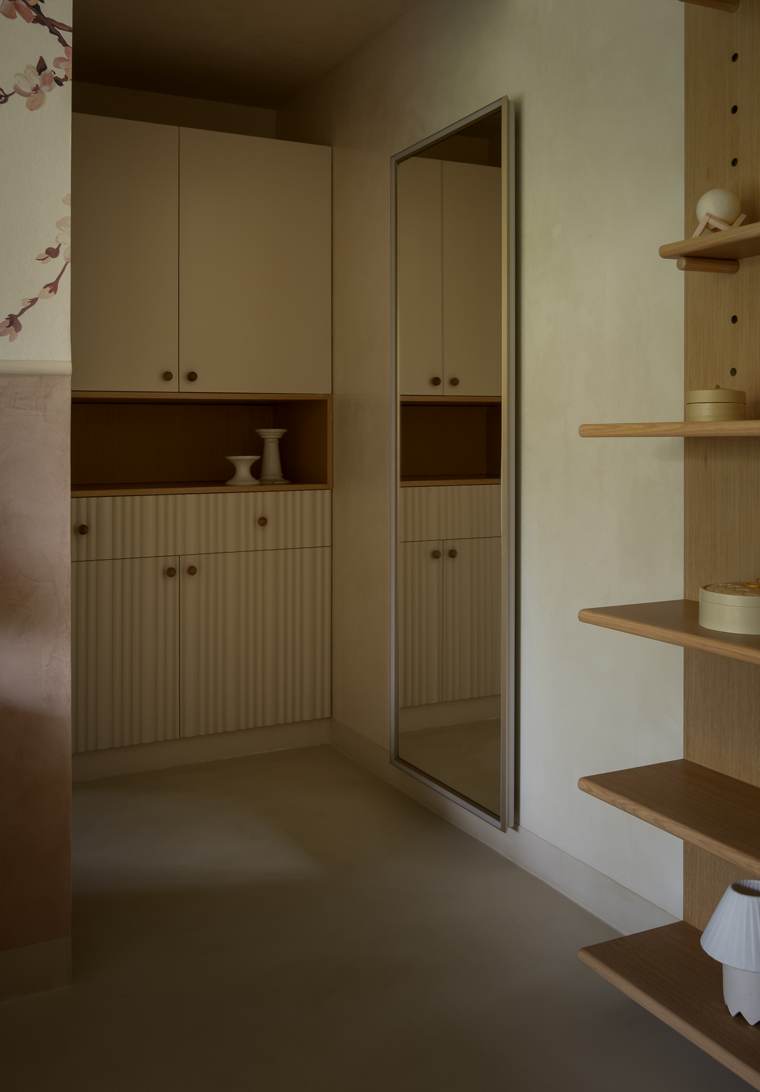 Child's room corner with built-in cabinets with fluted lower doors, a tall mirror, oak shelving with ceramic objects and cherry-blossom wallpaper at the left edge
