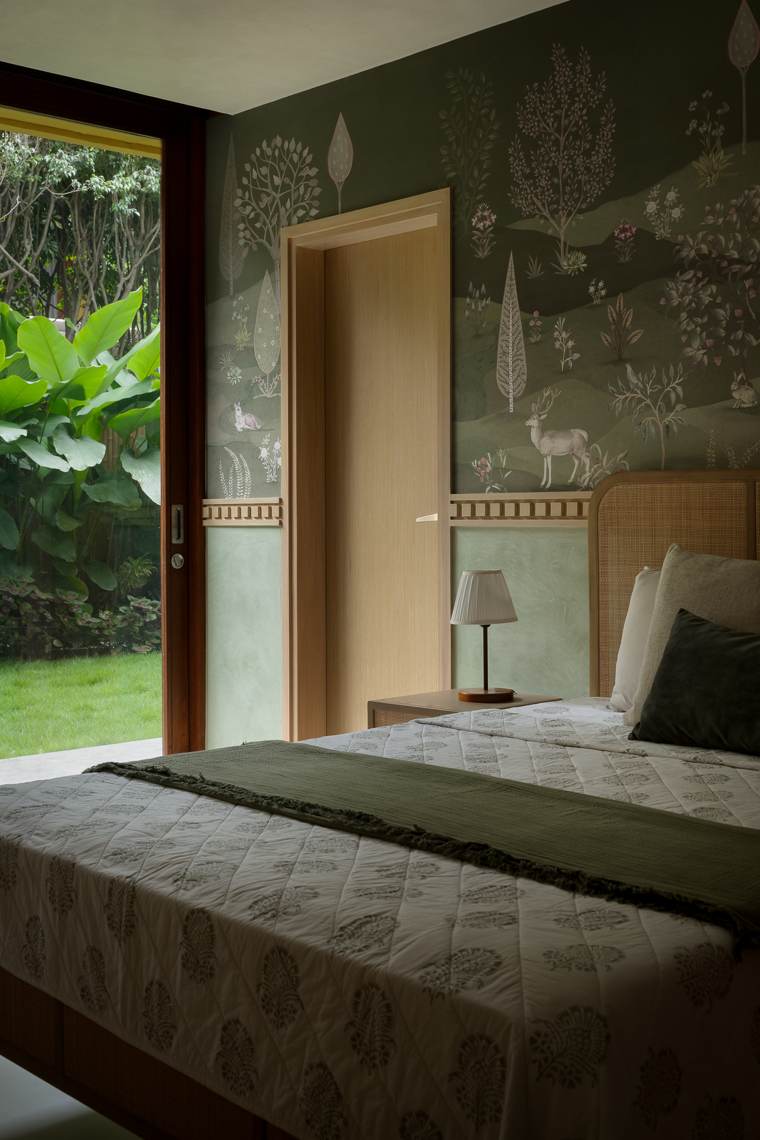 Bedroom with a deer-and-trees woodland wallpaper, a fluted-edge oak door, a cane bedhead and a sliding door to a garden