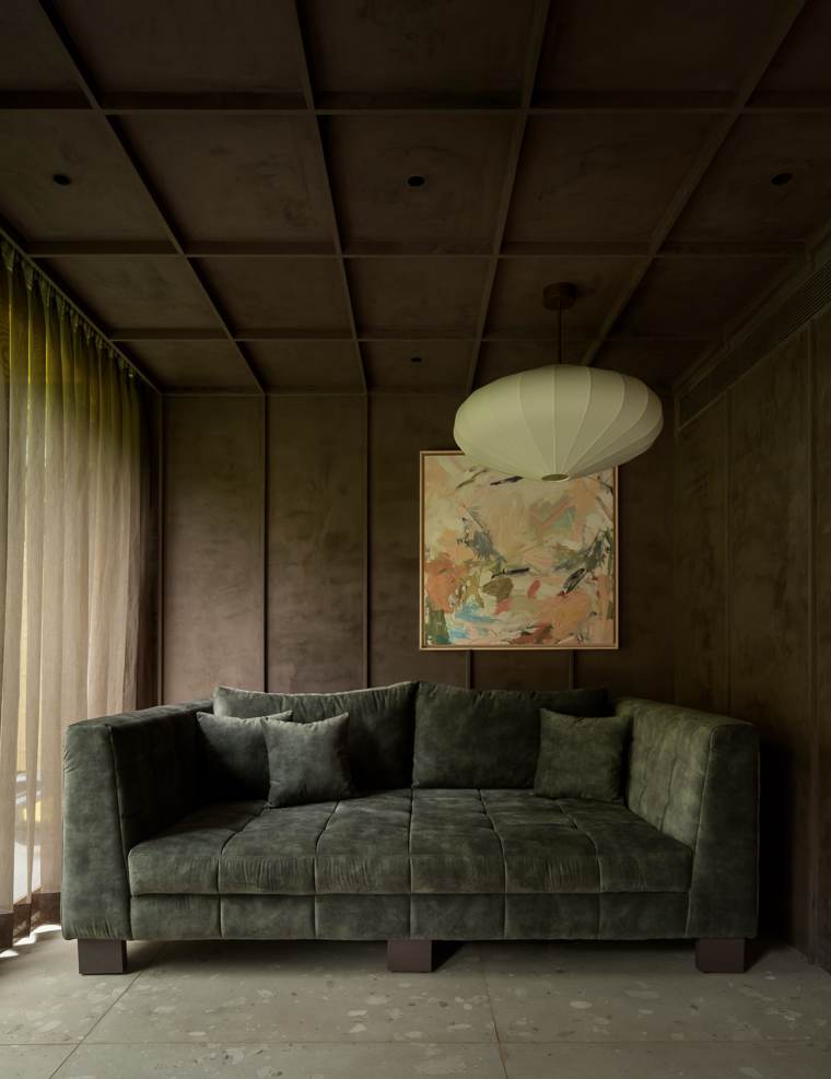 Den with a dark olive velvet sofa, a coffered plaster ceiling, an abstract painting, a cream pendant and sheer curtains on a terrazzo floor
