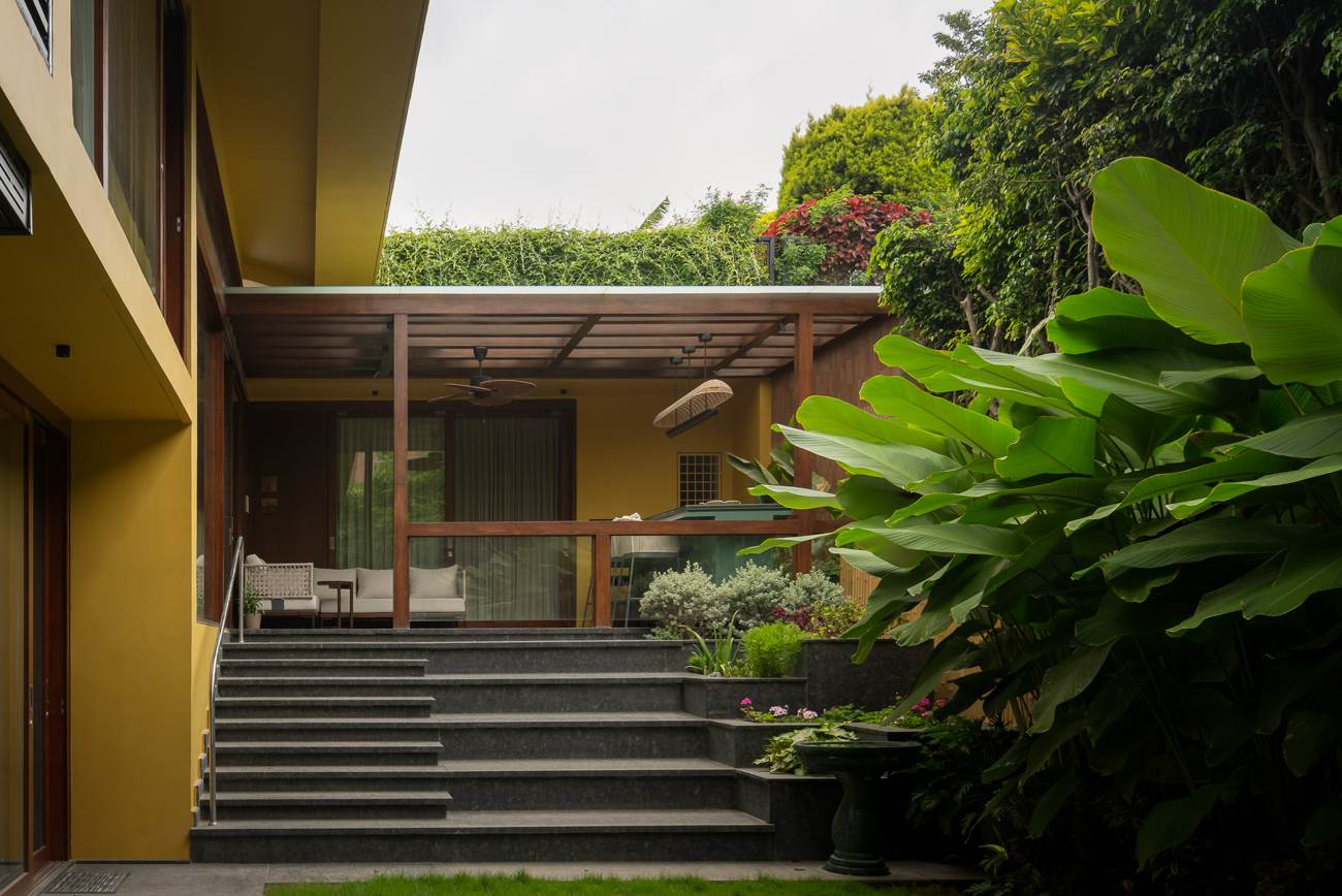 Granite steps rising to a covered timber pergola terrace with a ceiling fan and yellow walls, framed by large banana leaves and garden greenery