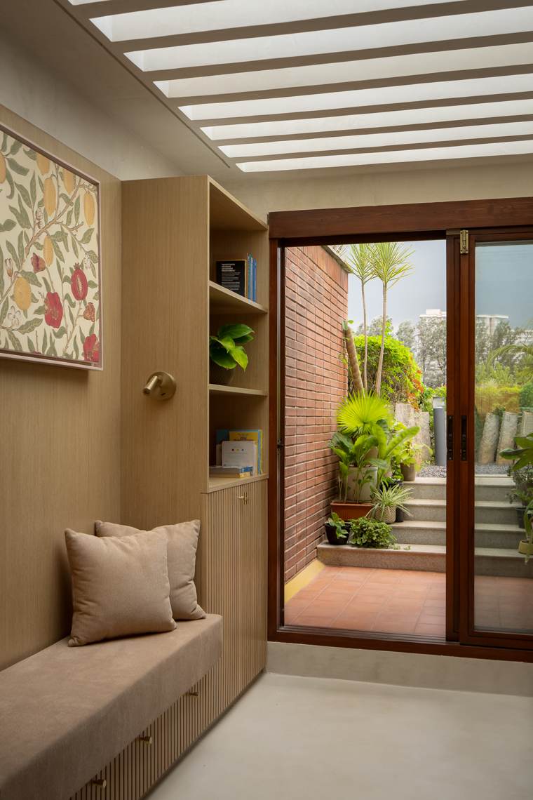 Built-in timber bench with tan cushions and fluted storage beneath open shelves, a framed pomegranate print and a skylight over a doorway to a brick-walled courtyard
